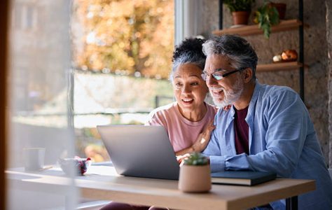 Surprised senior couple sitting together at home, gazing at their laptop screen, sharing in the joy of good news and experiencing a moment of happiness and connection
